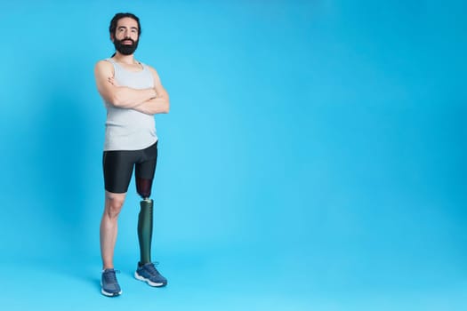 Studio portrait with blue background of a man with a leg prosthesis standing with arms crossed