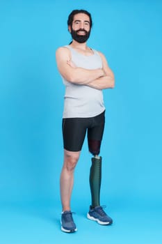 Vertical studio portrait with blue background of a sportive man with a leg prosthesis standing with arms crossed