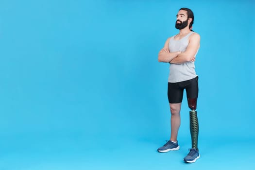 Studio portrait with copy space and blue background of a man standing with a metal prosthesis on his leg with his arms crossed