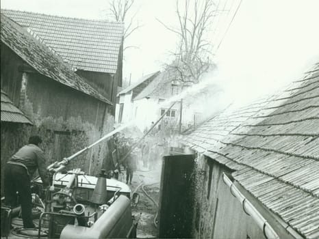 THE CZECHOSLOVAK SOCIALIST REPUBLIC - CIRCA 1980s: Retro photo shows fireman stands on the top of fire truck. Fireman demonstrates fire hose handling during a damage control exercise. Vintage black and white photography.