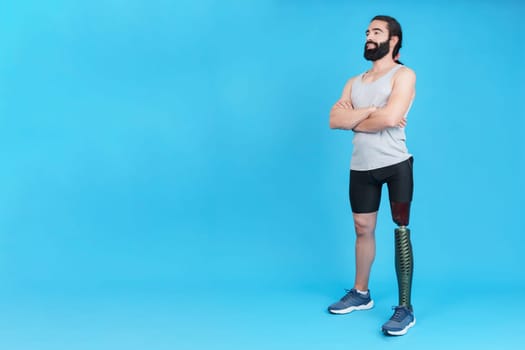 Studio portrait with blue background of a man with his arms crossed standing with a leg prosthesis
