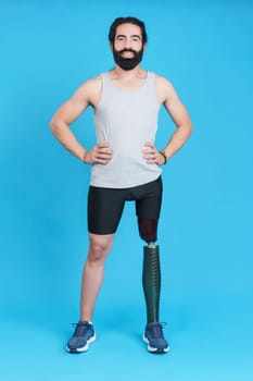 Vertical Studio portrait with blue background of a man standing with a leg prosthesis looking at camera