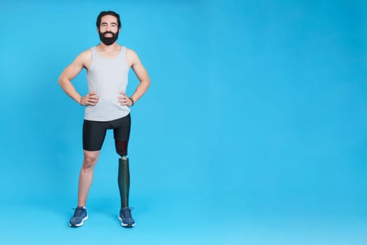 Studio portrait with copy space and blue background of a smiley man standing with a leg prosthesis
