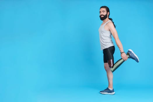 Studio portrait with copy space and blue background of the profile of a man with a prosthesis on his leg stretching