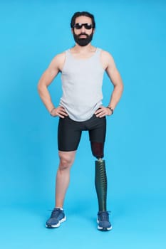 Vertical Studio portrait with blue background of a sportive stylish man with sunglasses standing with a prosthetic leg