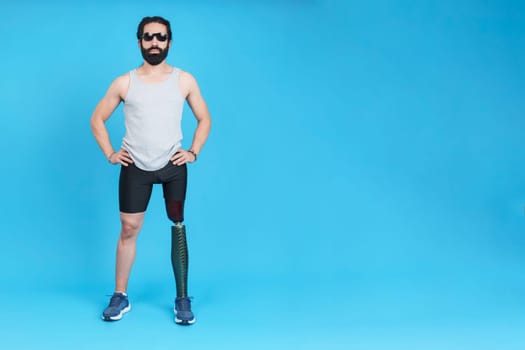 Studio portrait with blue background of a bearded man with sunglasses and a prosthetic leg