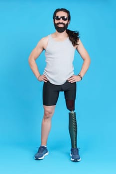 Vertical Studio portrait with blue background of a smiley man with sunglasses standing with a prosthetic leg