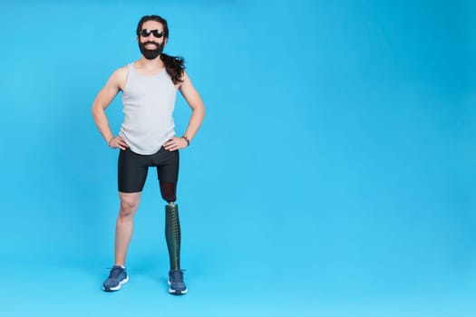 Studio portrait with blue background of a happy man with a prosthesis in the leg and sunglasses looking at camera