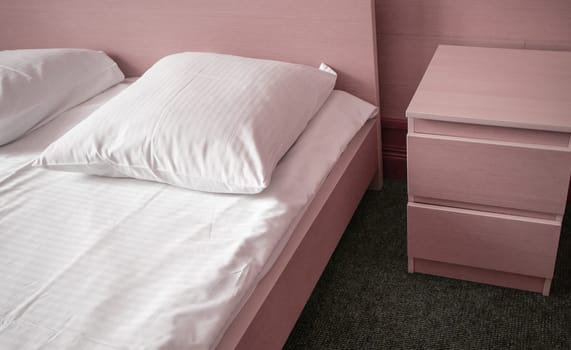 Soft pink tinting, close-up of the bed and bedside table, modern interior of the bedroom in the hotel.