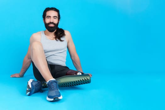 Studio photo with copy space and blue background of a relaxed sportive man with a leg prosthesis sitting on the floor