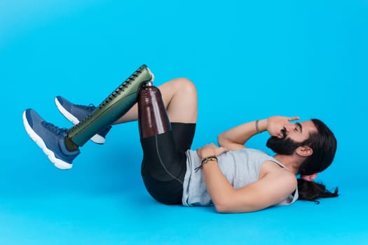 Horizontal studio portrait with blue background of a sportive man with a prosthetic leg doing sit-ups