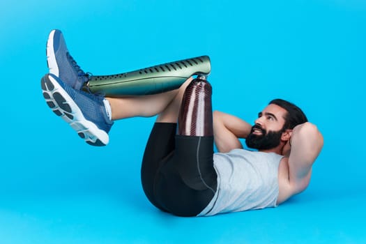 Horizontal studio portrait with blue background of a sportive man with a leg prosthesis doing abdominal crunches