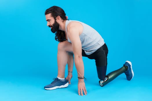 Horizontal studio portrait with blue background of a man with a leg prosthesis in sprinting position