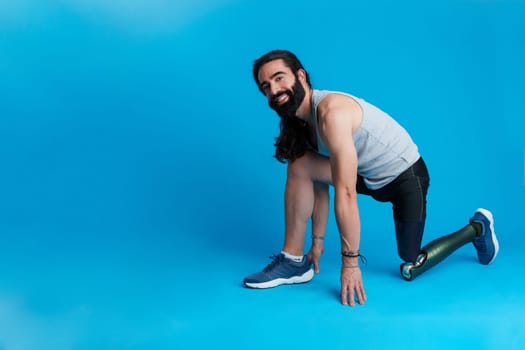Horizontal studio portrait with blue background and copy space of a man with a leg prosthesis in sprinting position