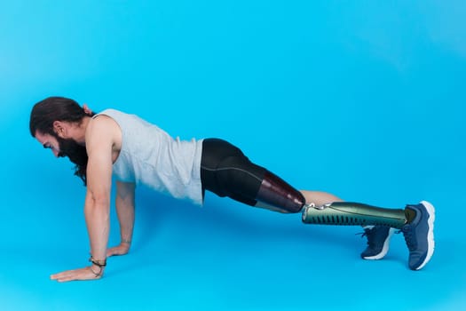 Horizontal studio portrait with blue background of the profile of a man with a prosthetic leg doing push ups