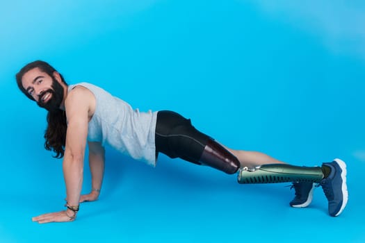 Horizontal studio portrait with blue background of a happy man with a prosthetic leg doing push ups