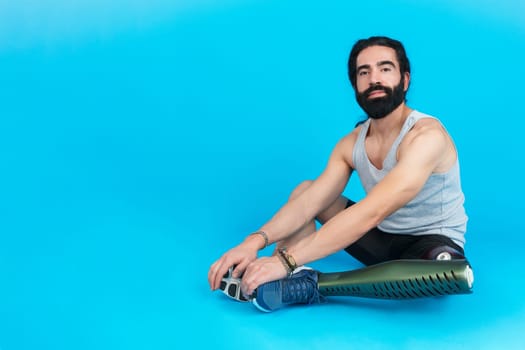 Horizontal studio portrait with blue background of a sportive man with a prosthetic leg sitting on the floor