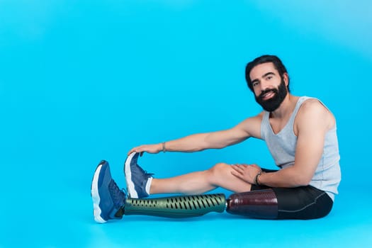 Studio photo with blue background and copy space of a sportive man with prosthetic leg looking at camera while stretching