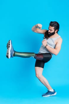 Vertical Studio portrait with blue background of a man with a prosthetic leg kicking and fighting