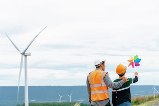 Engineer with his son holding windmill toy on a wind farm atop a hill or mountain. Progressive ideal for the future production of renewable, sustainable energy. Energy generated from wind turbine.