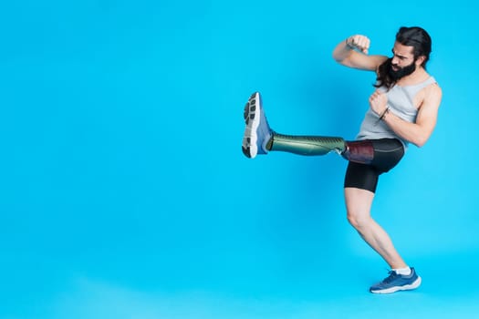 Studio portrait with blue background of a man with a prosthesis on his leg kicking and fighting