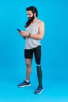 Vertical Studio portrait with blue background of a man with a leg prosthesis using a mobile