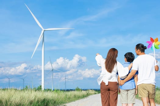 Concept of progressive happy family enjoying their time at the wind turbine farm. Electric generator from wind by wind turbine generator on the country side with hill and mountain on the horizon.