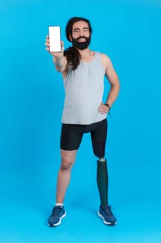 Vertical Studio portrait with blue background of a smiling man with a leg prosthesis showing a mobile screen