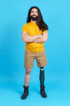 Vertical studio portrait with blue background man with prosthesis on the leg standing with arms crossed