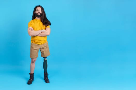 Studio portrait with blue background and copy space of a serious man with prosthesis on the leg standing with arms crossed