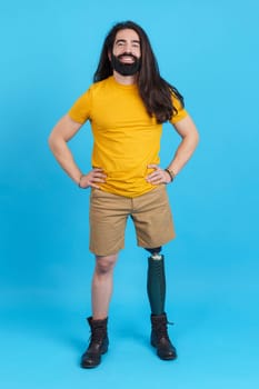 Vertical studio portrait with blue background of a man with a prosthesis on a leg smiling at camera