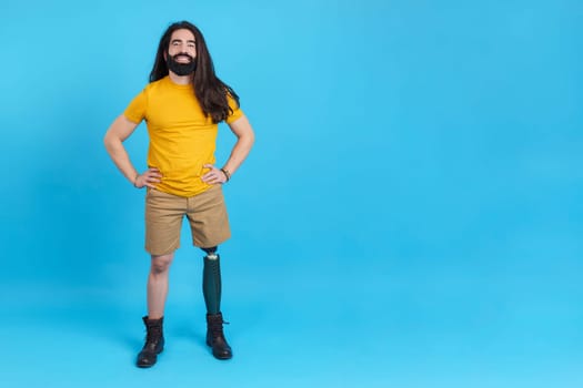Studio portrait with blue background and copy space of a relaxed man with a prosthesis on a leg standing smiling at camera