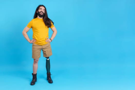 Studio portrait with blue background of a happy man with prosthesis leg smiling while posing