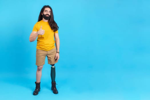 Studio portrait with blue background and copy space of a man with a prosthesis leg gesturing approval with the thumb up