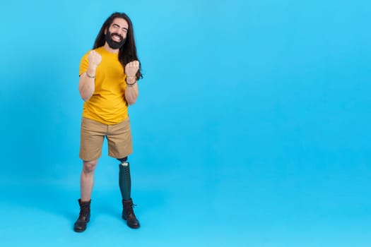 Studio portrait with blue background and copy space of a happy man with a leg prosthesis celebrating with fists in the air