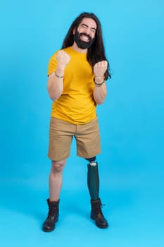 Vertical studio portrait with blue background of an emotional man with a leg prosthesis celebrating with fists