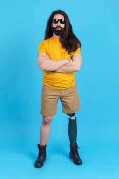 Vertical studio portrait with blue background of a rude man with a leg prosthesis looking at camera with the arms crossed