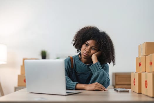 Stressed young entrepreneur African American woman and courier parcel box at home office. Small business owner, online market delivery, lifestyle freelance concept.