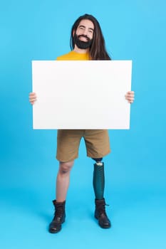 Vertical studio portrait with blue background of a man with prosthetic leg holding a poster in white