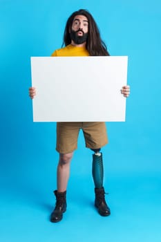 Vertical studio portrait with blue background of a man with prosthetic leg holding a blank canvas