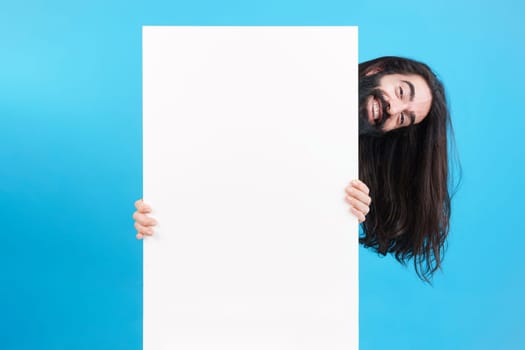 Studio portrait of a happy playful man with long hair holding a board with blank space
