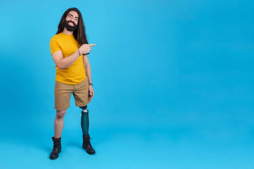 Studio portrait with blue background and copy space of a man with prosthetic leg pointing to the empty space at the side