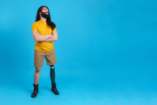Studio portrait with blue background and copy space of a smiling man with prosthetic leg looking to the copy space aside