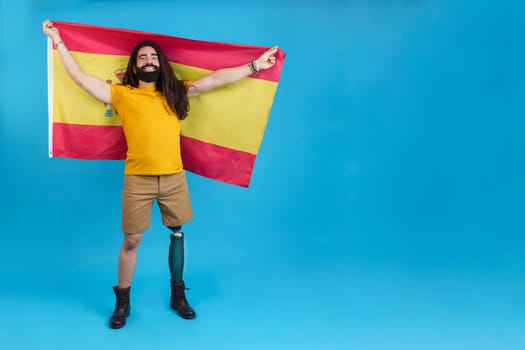 Studio portrait with blue background and copy space of a man with prosthetic leg raising a Spanish flag