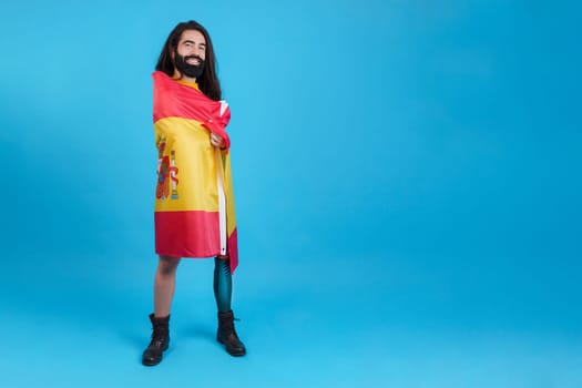 Studio portrait with blue background of a man with prosthetic leg wrapped in a spanish national flag