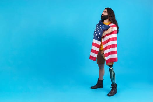 Studio portrait with blue background of a man standing with prosthetic leg wrapped in a north america national flag