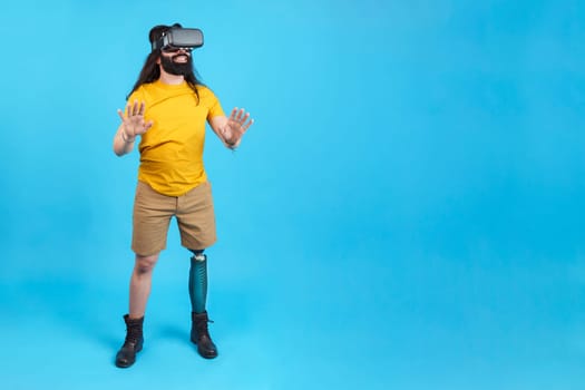 Studio portrait with blue background and copy space of a man with prosthetic leg gesturing while using a virtual goggles