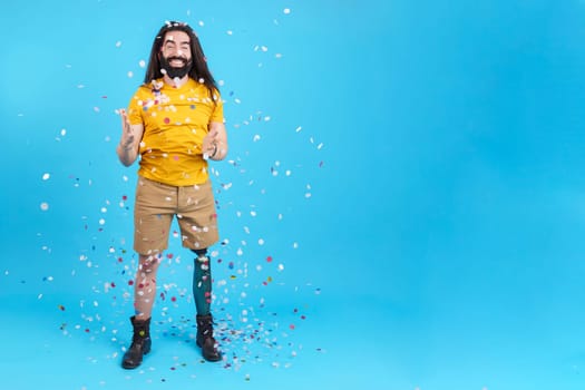 Studio portrait with blue background and copy space of a happy man with a leg prosthesis surrounded by flying confetti