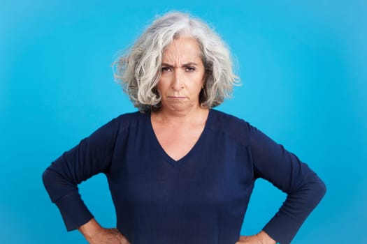 Studio portrait with blue background of a mature woman looking at camera with an upset expression