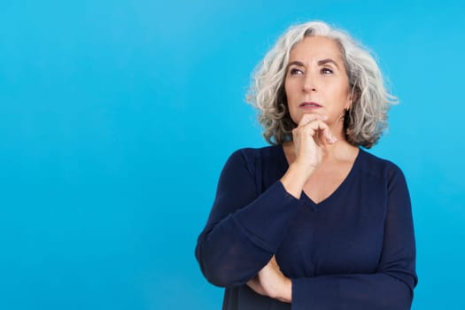 Studio portrait with blue background of a mature woman gesturing and looking up with pensive expression